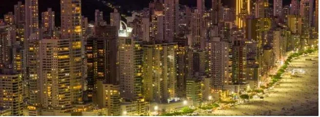 Vista aérea noturna de Balneário Camboriú com os prédios iluminados à beira-mar